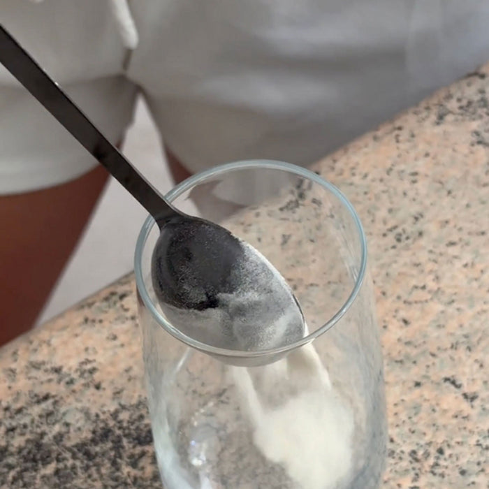 Collagen powder being spooned into a glass on a speckled countertop.