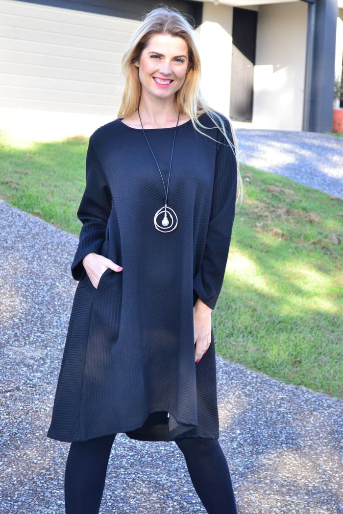 Black textured tunic dress by Poney featuring a relaxed fit and soft fabric, displayed hanging on a wooden hanger.