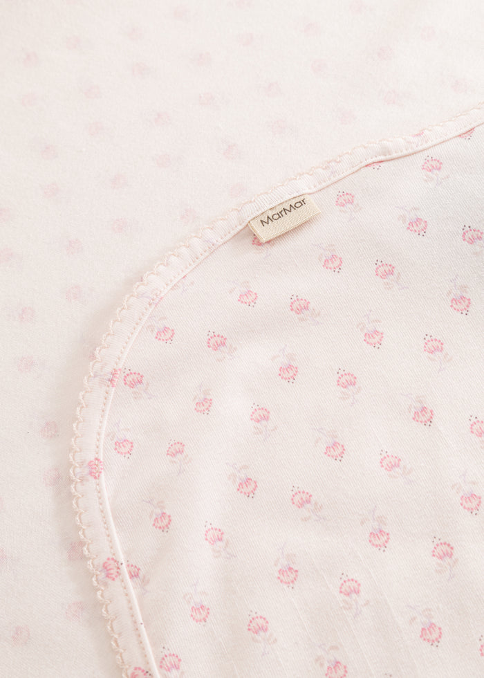 Mini rug with pink floral pattern, slanted seam edges and a small tag.