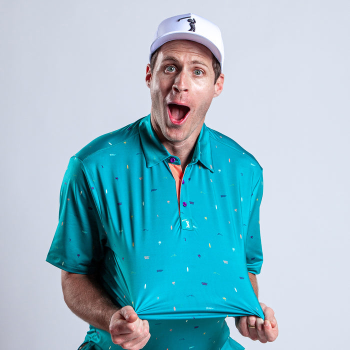A man in a Beach - Polo, a teal golf shirt with multicolored specks and athletic fit, pulls his shirt out with both hands, mouth open in surprise. Its moisture-wicking fabric keeps him cool against a plain light gray background.