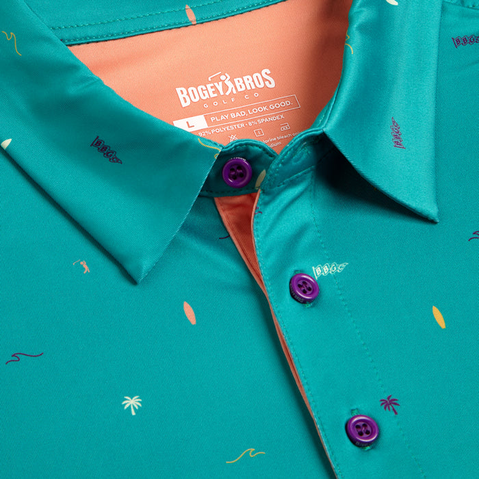 Close-up of the Beach - Polo, a teal golf shirt with an all-over orange and purple surfboard, palm tree, and wave pattern. Features purple buttons, orange inner collar, athletic fit, and moisture-wicking comfort.