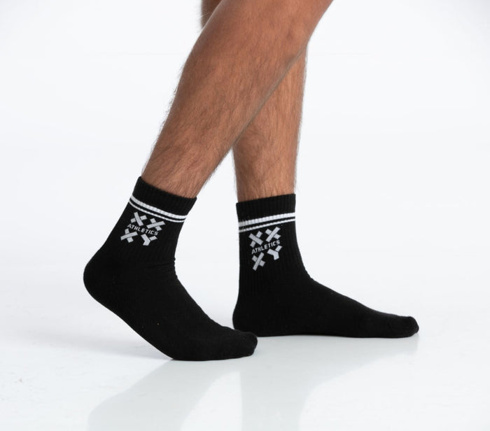 A pair of black Candid crew half calf socks with a white cross pattern on the cuff, worn on male legs against || Black