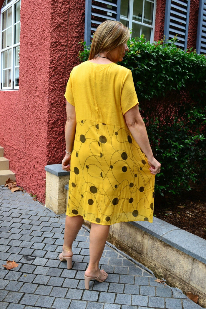 Wishstone Dotty Yellow Pocket Dress Tunic hanging on a hanger, featuring a bright yellow fabric with playful dot patterns and a front pocket.