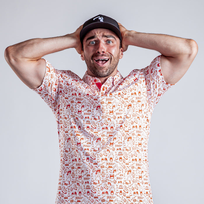 A man in the Glizzy Gobbler - Polo and a black cap stands against a light gray background, holding his head with both hands, eyes wide and mouth open in a surprised expression.