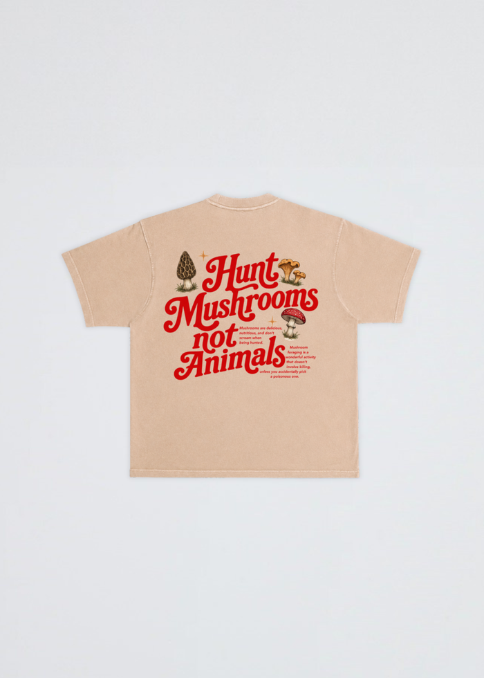 A beige short-sleeve t-shirt shown flat against a light gray background, featuring a graphic on the back with the text 'Hunt Mushrooms not Animals' in red, accompanied by illustrations of a morepenny and mushrooms.