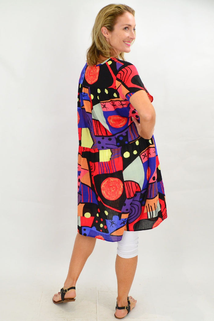 Hourglass Ken Done Inspired Peasant Tunic Dress with colorful floral pattern and relaxed fit, displayed on a hanger.