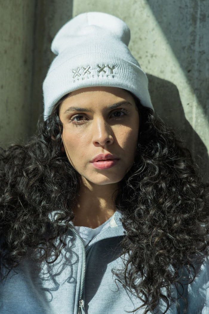Woman wearing a white beanie and light blue jacket against a concrete wall. || white