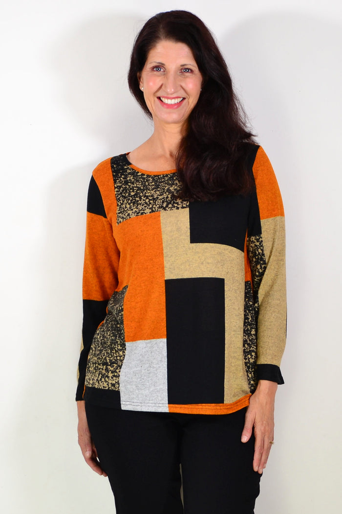 Orange and black geometric print Hourglass tunic top displayed on a hanger, showcasing its vibrant pattern and stylish design.