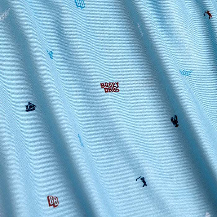 The Port - Polo features light blue, soft-textured fabric with an athletic fit, moisture-wicking properties, and small embroidered golf-themed icons like lobsters, sailboats, golf clubs, plus red BOGEY BROS text scattered throughout.