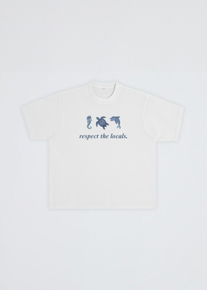 A white short-sleeve crewneck t-shirt featuring a blue graphic of three sea creatures (seahorse, turtle, dolphin) above the text 'respect the locals.' on the chest, displayed flat against a light gray background.