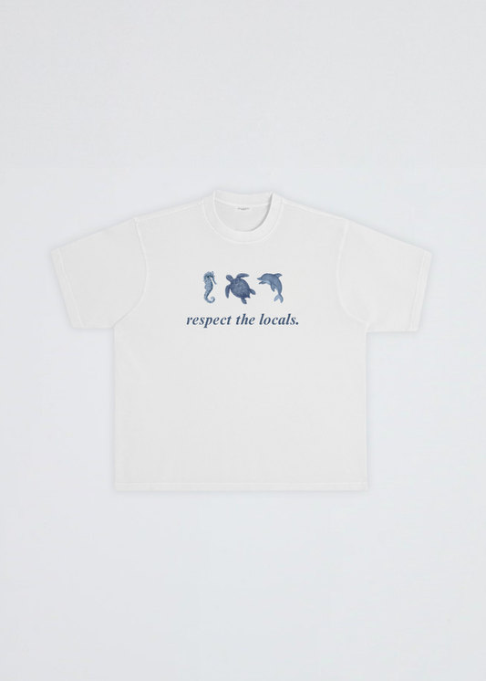 A white short-sleeve crewneck t-shirt featuring a blue graphic of three sea creatures (seahorse, turtle, dolphin) above the text 'respect the locals.' on the chest, displayed flat against a light gray background.