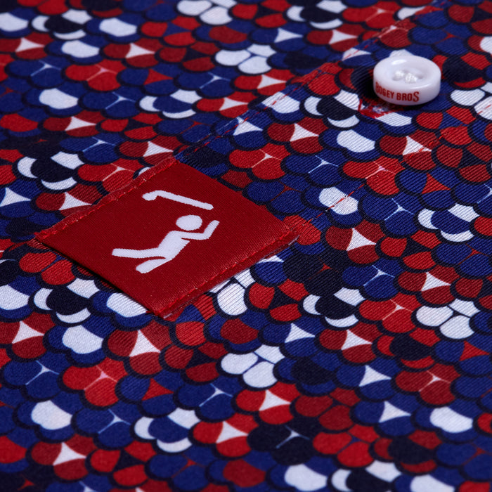 The Whale Tail - Freedom Cheeks - Polo showcases red, white, and blue scale-patterned fabric with a barbell tag. Its athletic fit and moisture-wicking design offer comfort, while a bold white “GET BROS” button completes the look.