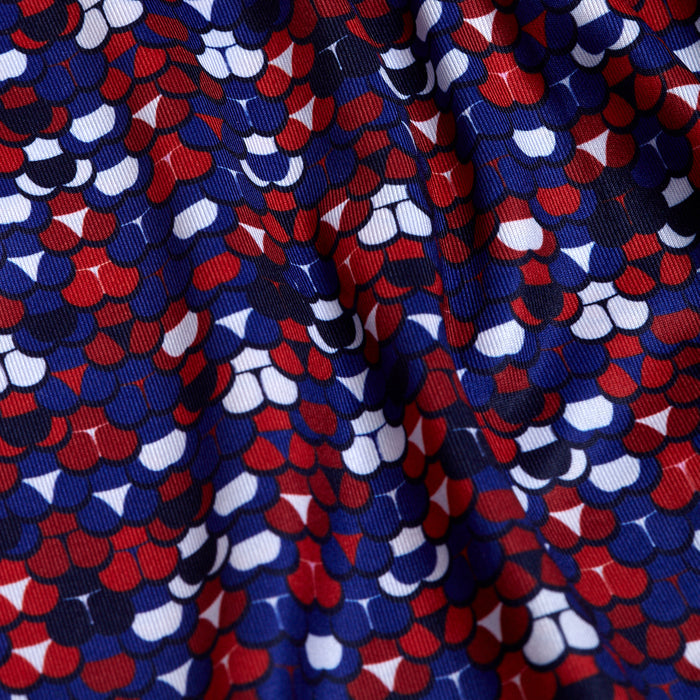 A close-up of the Whale Tail - Freedom Cheeks - Polo fabric shows a vibrant geometric pattern with red, white, and blue semi-circles. The slightly wrinkled texture adds depth while offering UPF 50 protection for safe outdoor wear.
